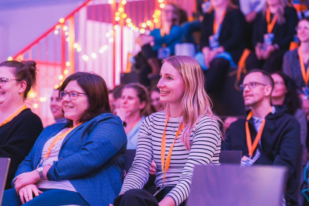 Mehrere Personen sitzen auf einer Tribüne, einige Lächeln.