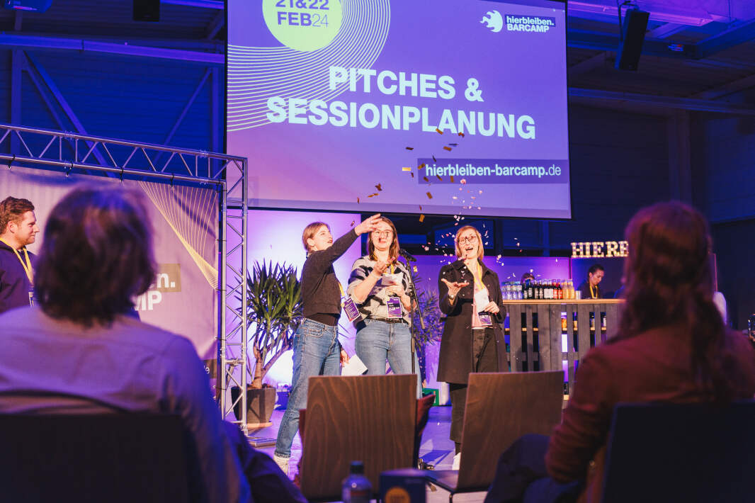 Drei Frauen stehen vor einer Leinwand und werfen mit Konfetti, sie lachen.