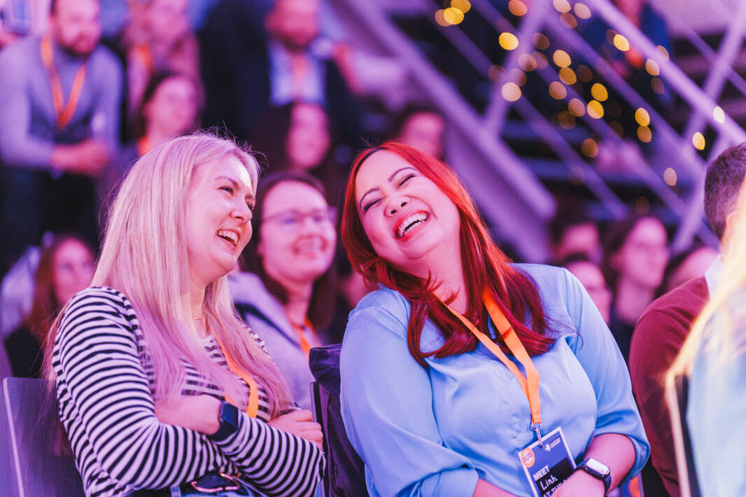 Zwei Frauen sind im Vordergrund eines Publikums zu sehen. Sie lachen miteinander.